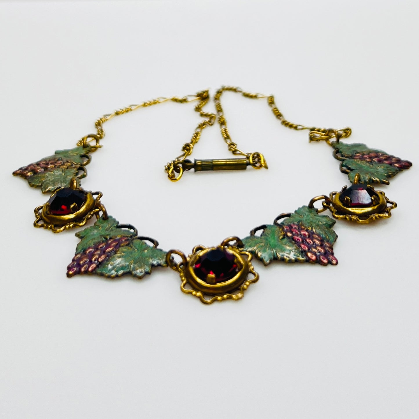 Side view of vintage enamel grape necklace with alternating rhinestone and leaf panels.
