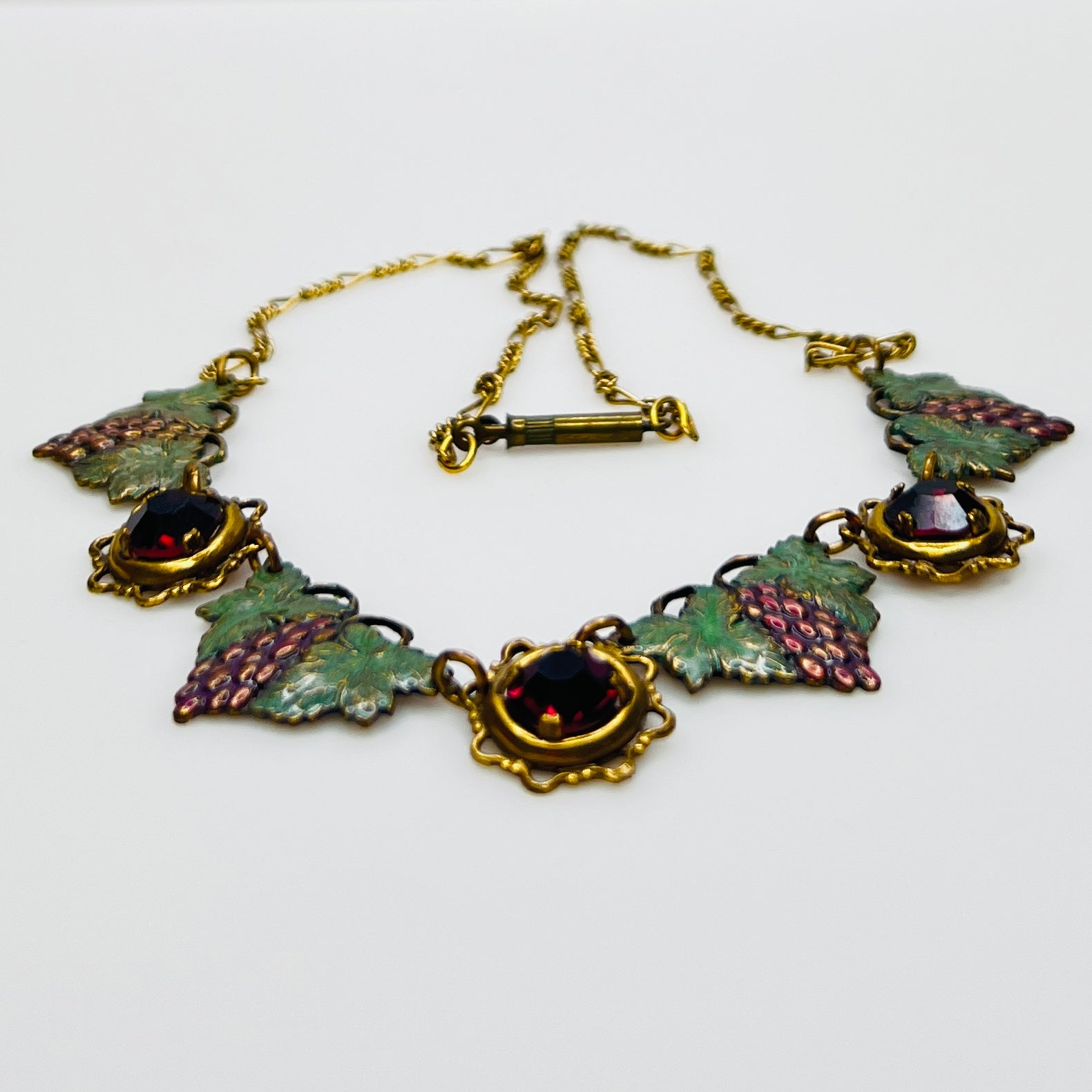 Side view of vintage enamel grape necklace with alternating rhinestone and leaf panels.