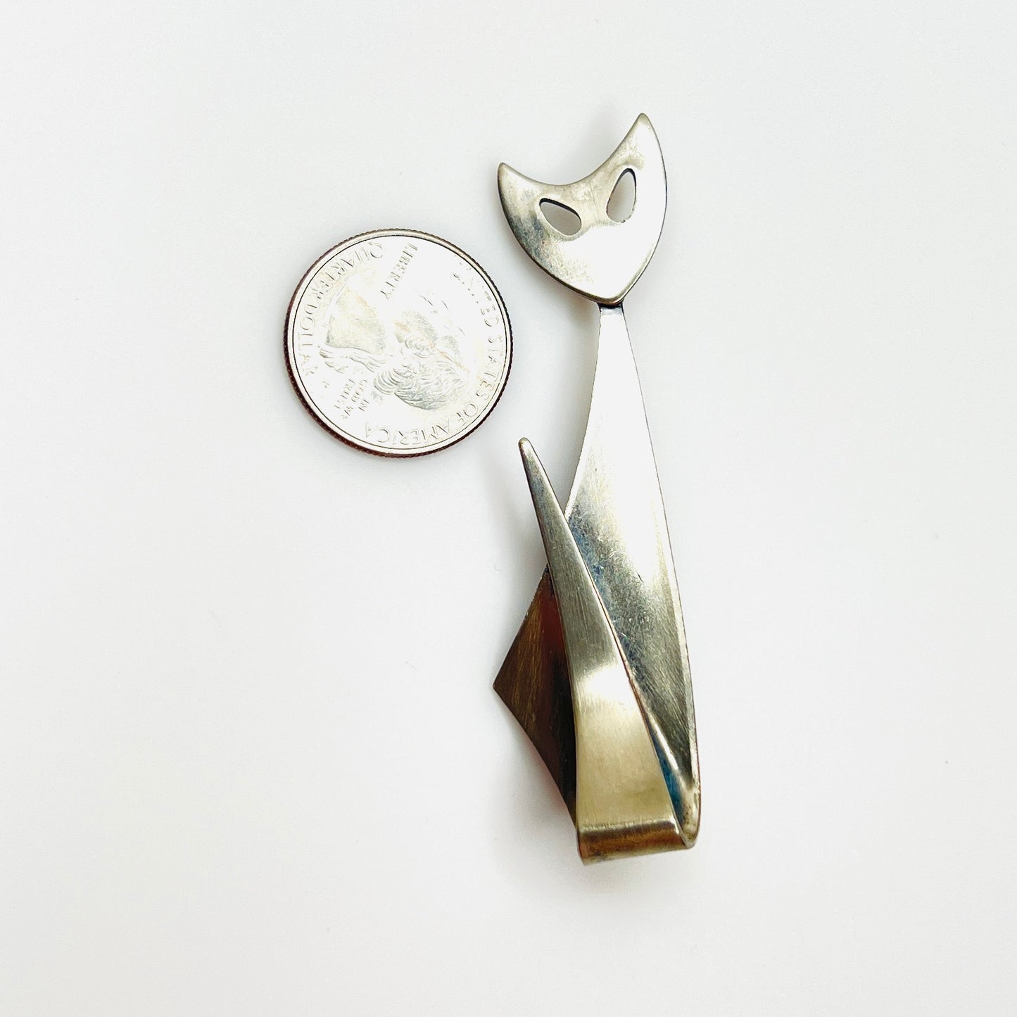Artisan stainless steel cat brooch beside quarter showing size and sleek Modernist silhouette.