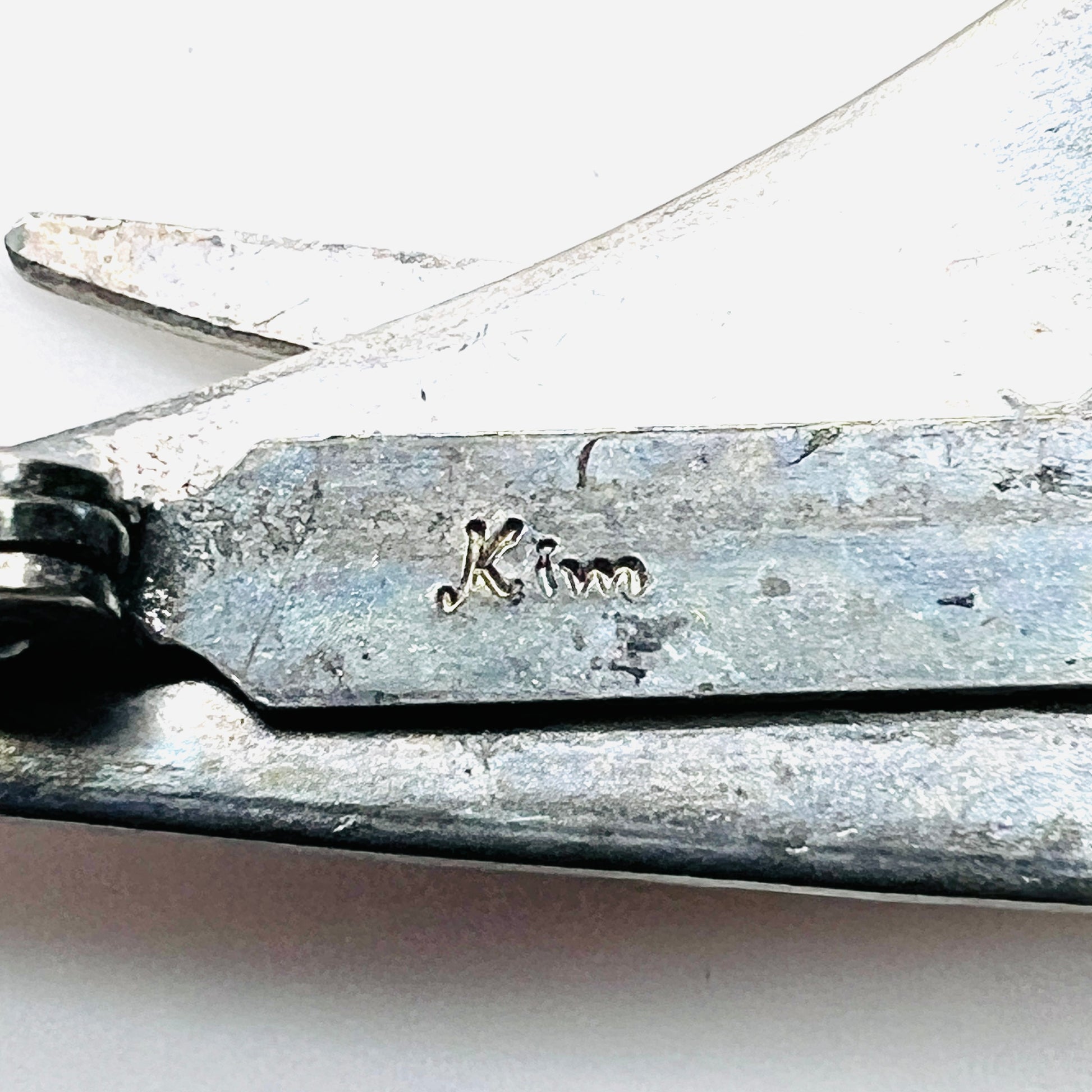 Close-up of Kim signature on vintage artisan stainless steel cat brooch.