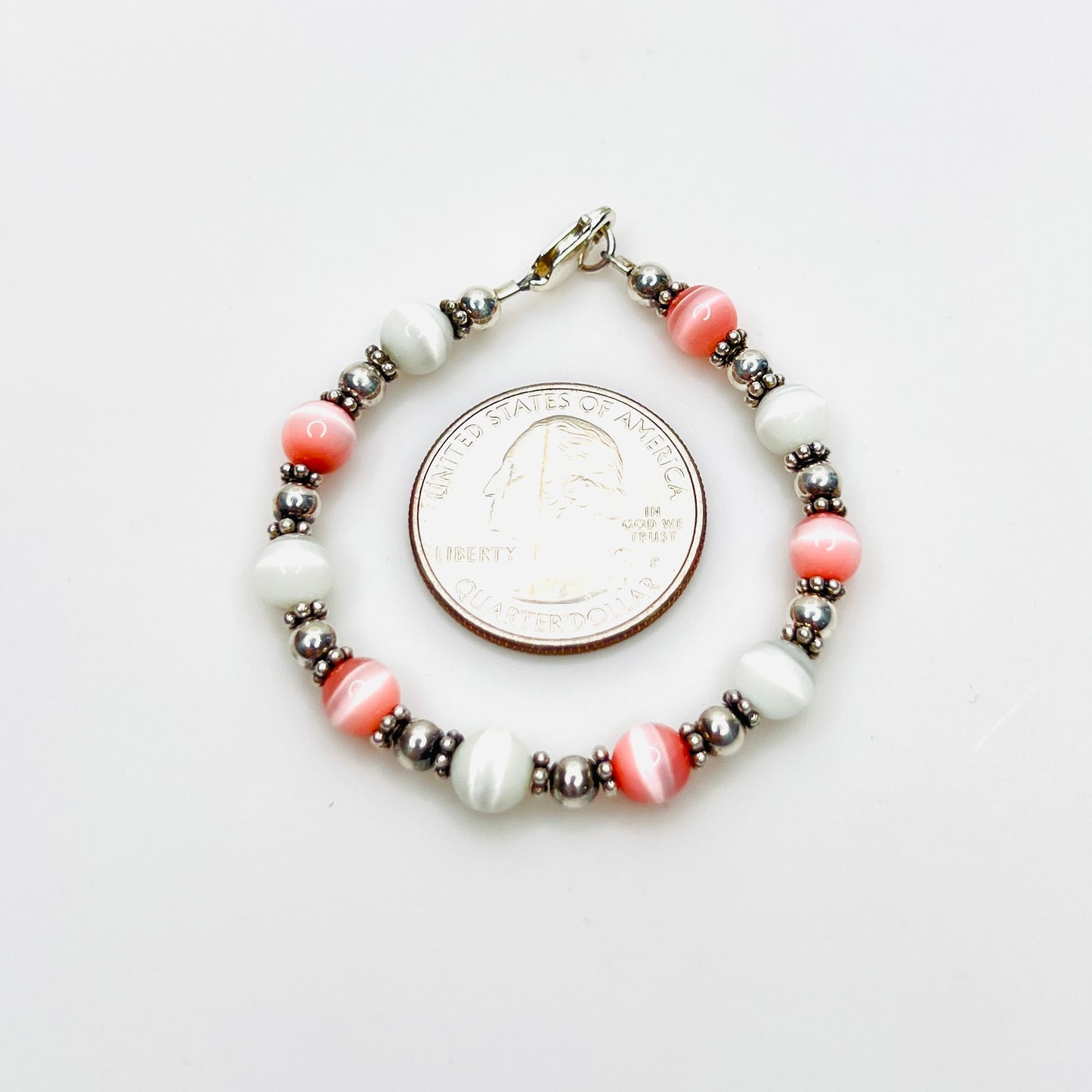 Pink and white cat's eye bracelet shown with quarter for scale