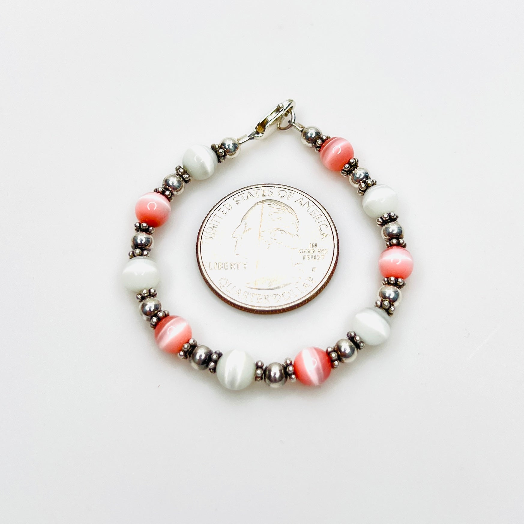Pink and white cat's eye bracelet shown with quarter for scale