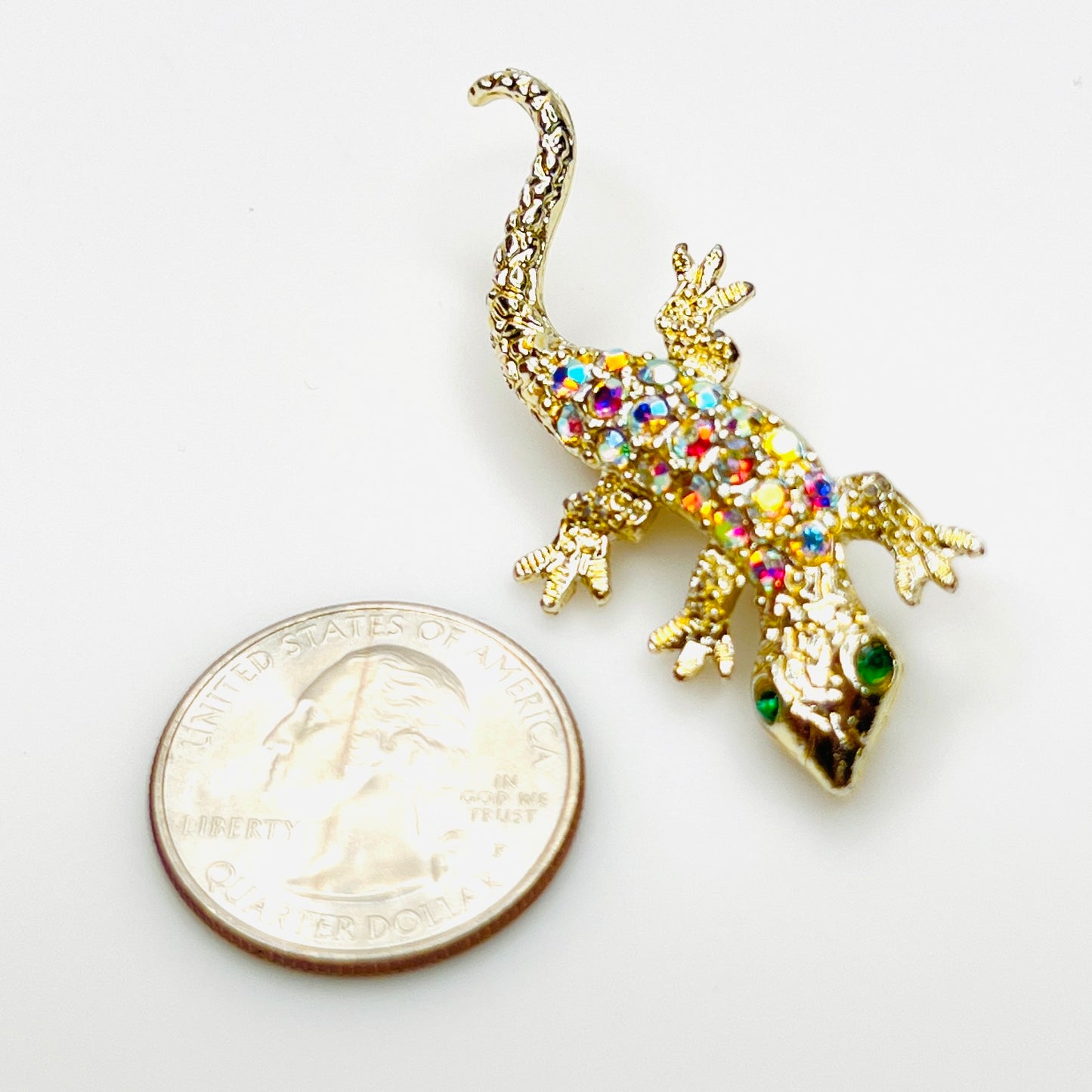 Gold-tone gecko brooch with aurora borealis rhinestones beside a U.S. quarter for size.