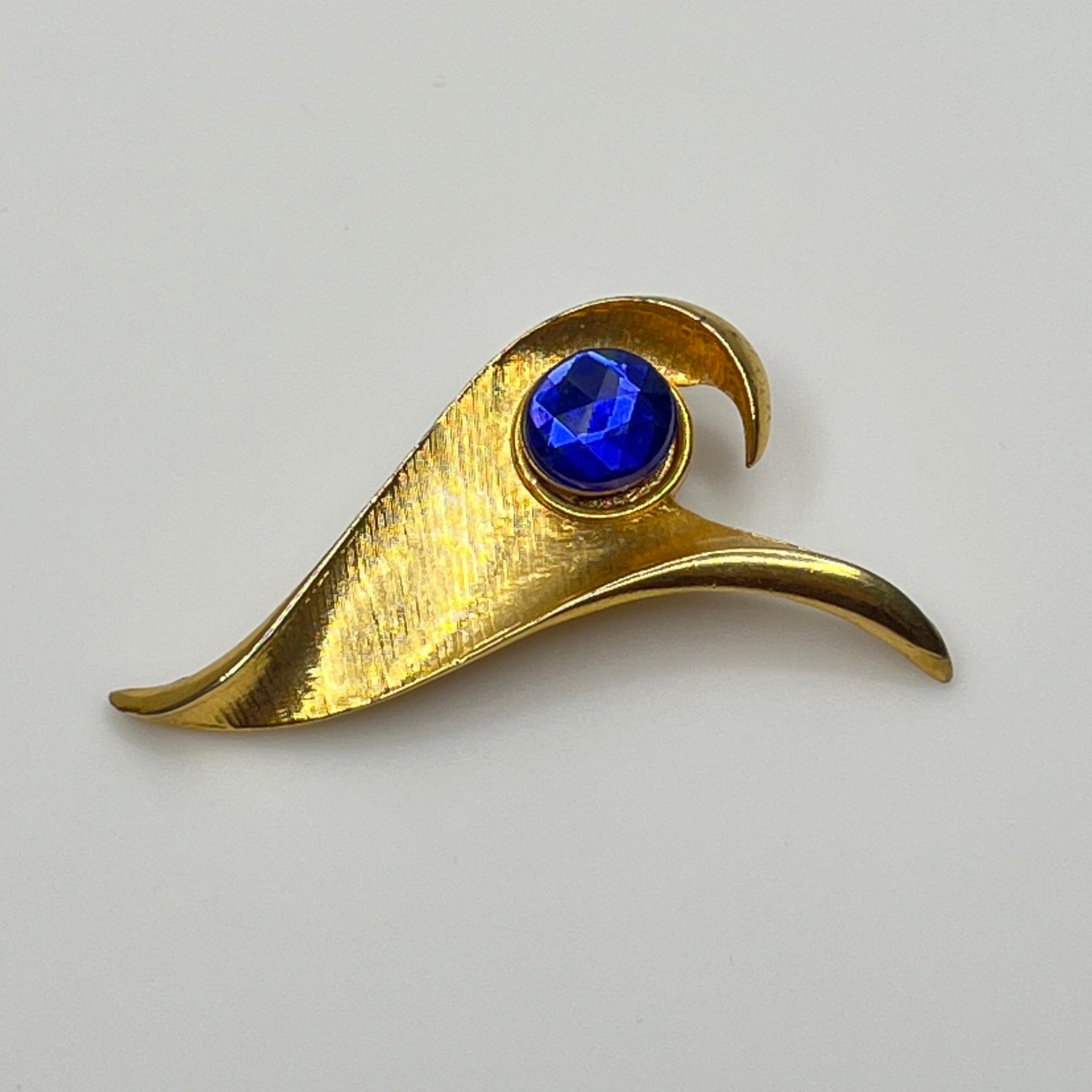 Modernist gold-tone brooch with sculptural wave shape and cobalt blue rhinestone center