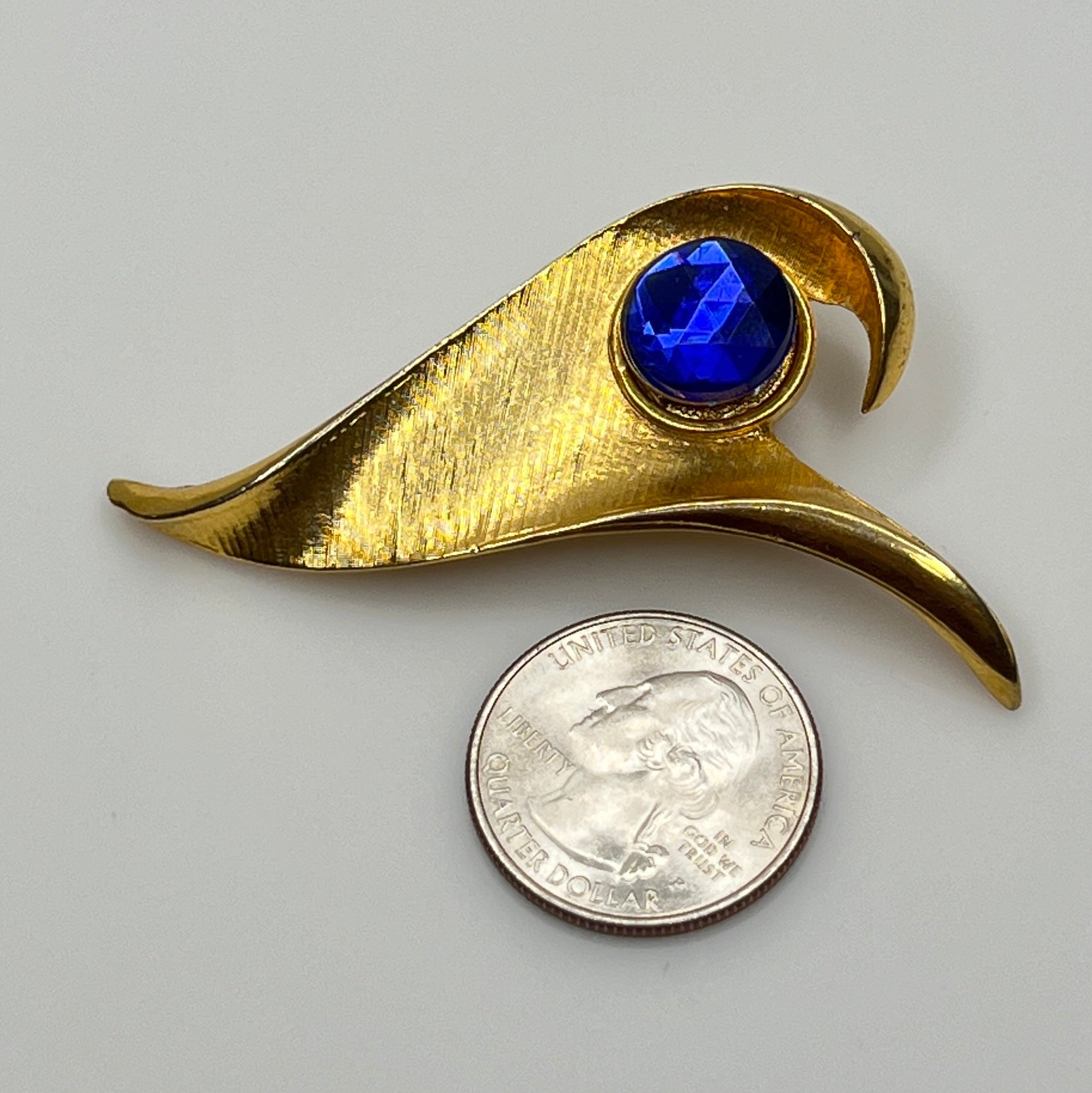 Modernist gold-tone brooch with sculptural wave shape and cobalt blue rhinestone center