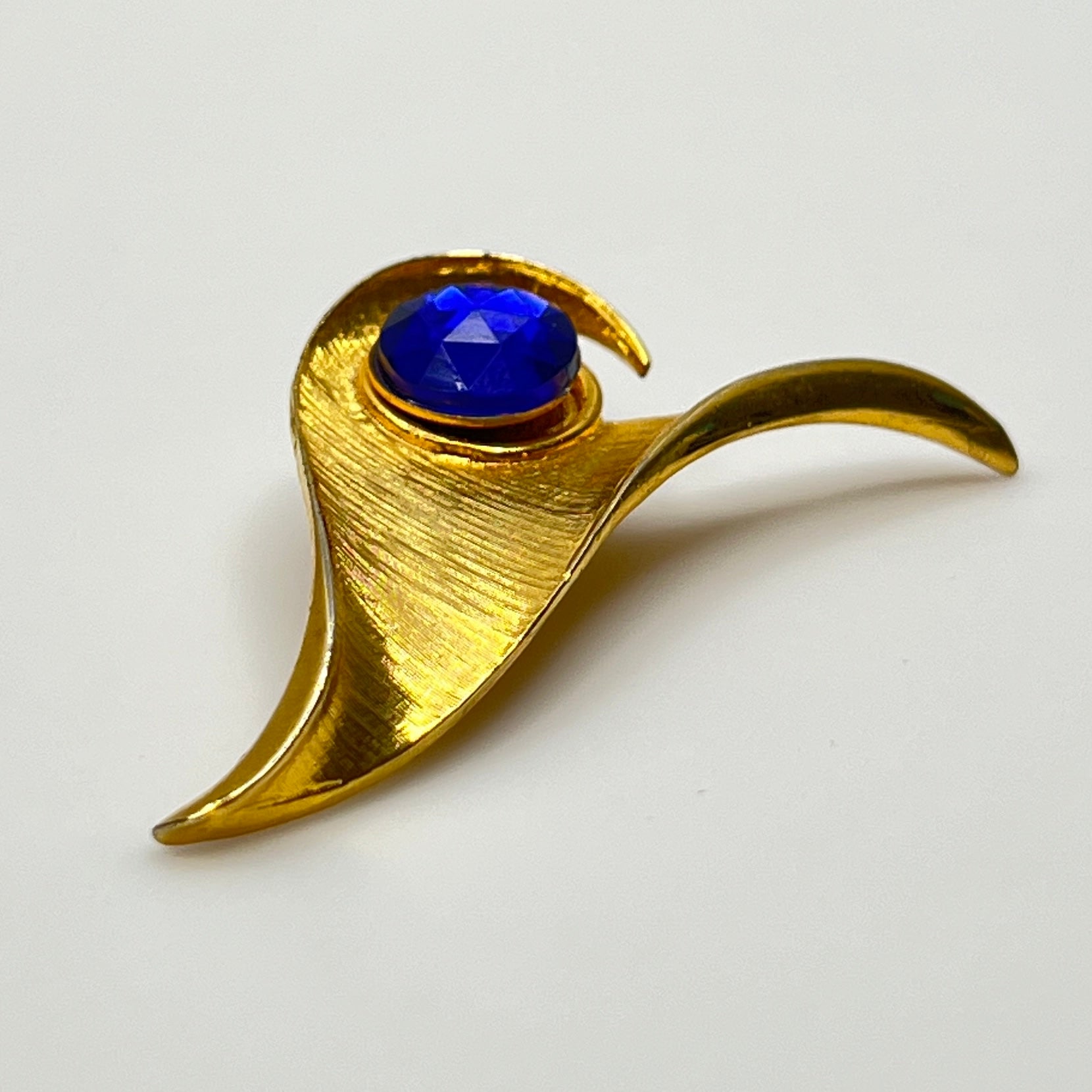 Modernist gold-tone brooch with sculptural wave shape and cobalt blue rhinestone center