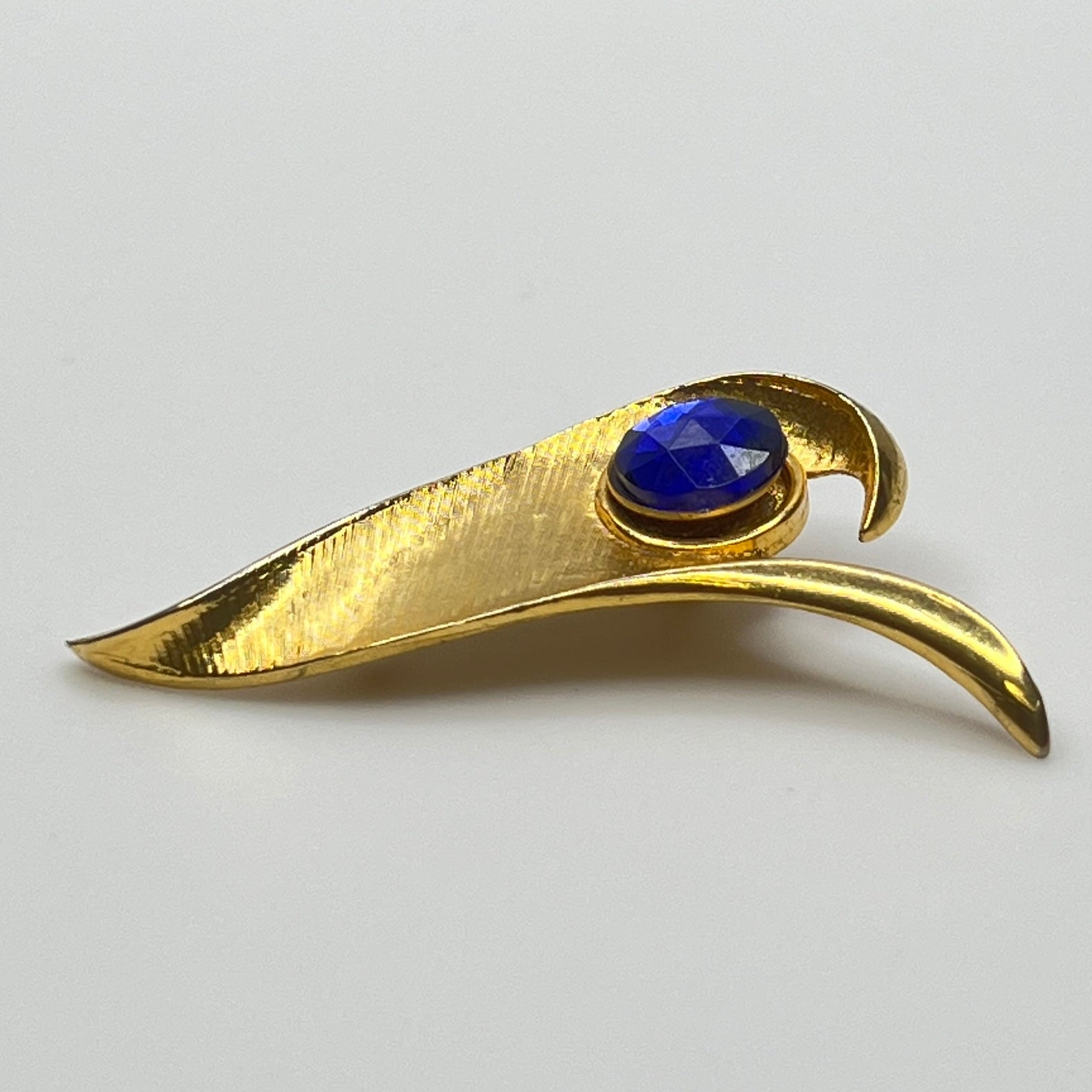 Modernist gold-tone brooch with sculptural wave shape and cobalt blue rhinestone center