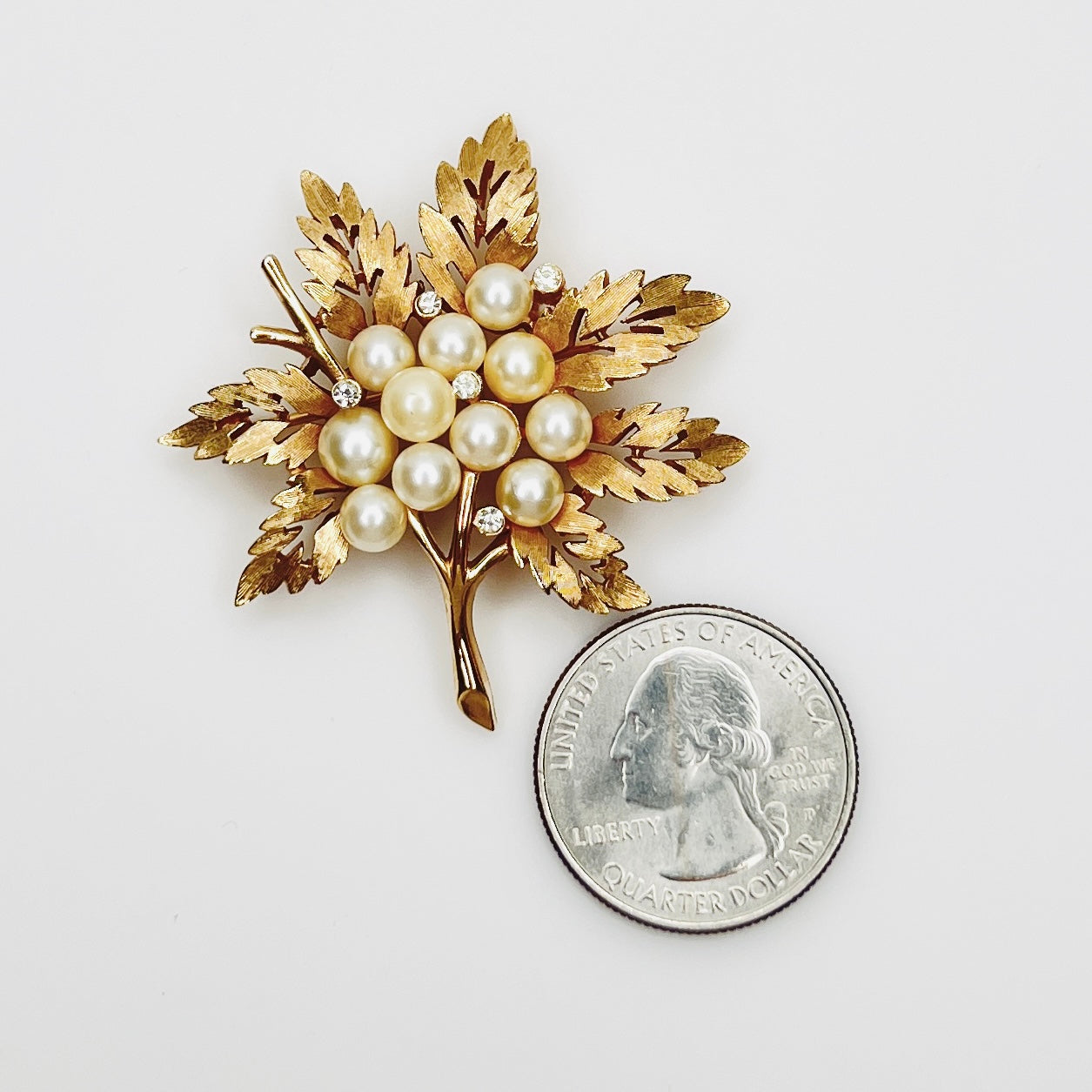 1950s Trifari pearl and rhinestone botanical brooch beside quarter for scale