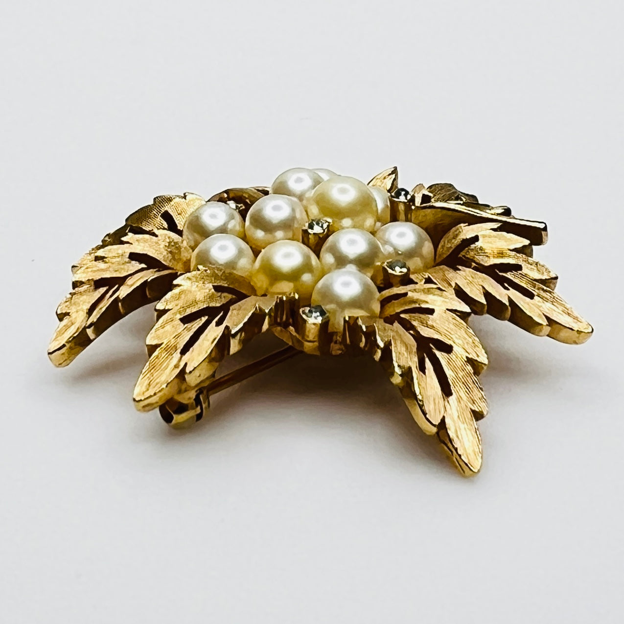 Side view of vintage Crown Trifari gold leaf brooch with faux pearls