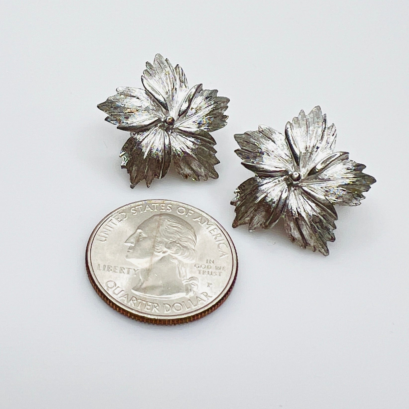 Textured silver tone Trifari floral earrings beside quarter