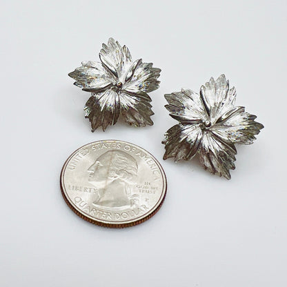 Textured silver tone Trifari floral earrings beside quarter