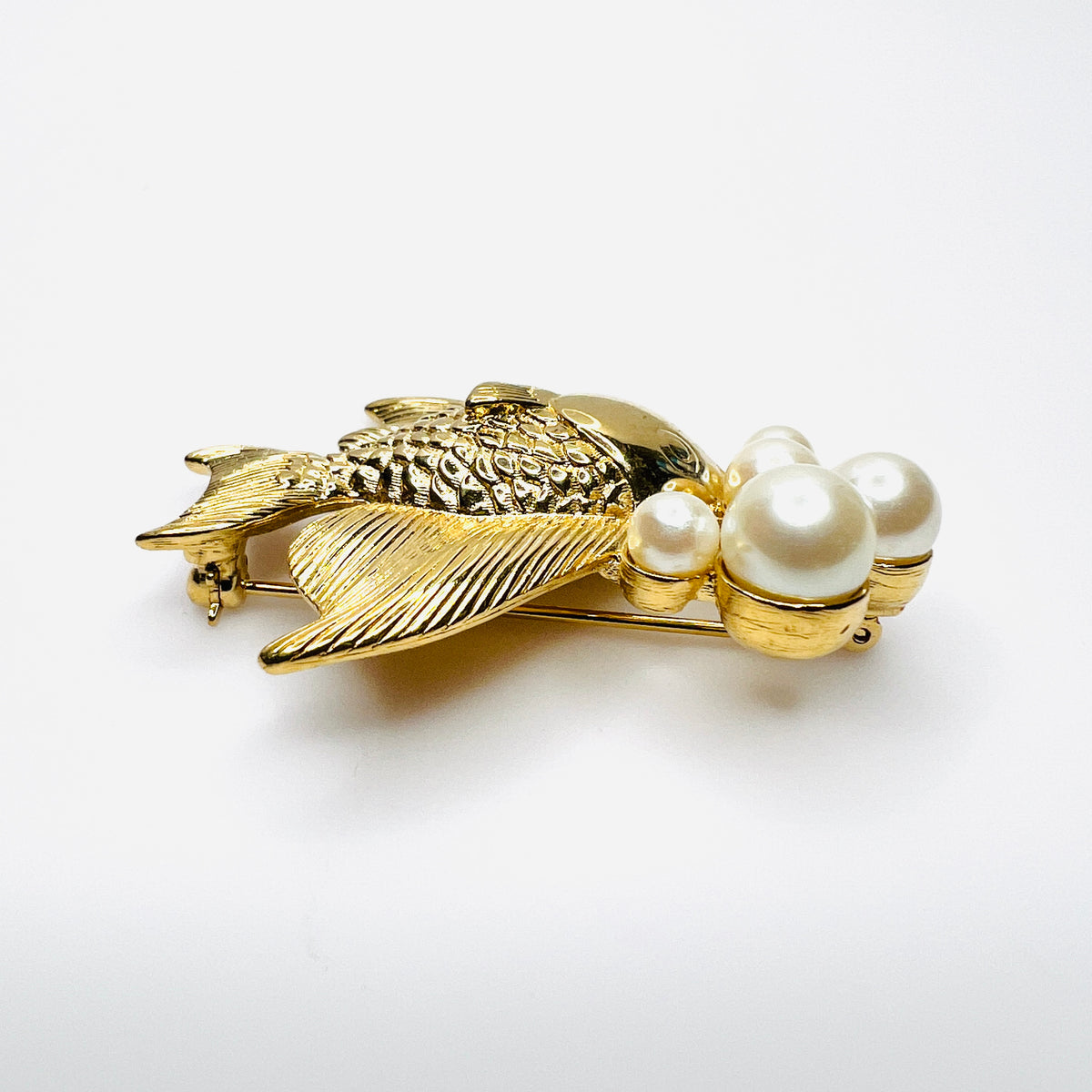 Side view of dimensional gold tone fish brooch with creamy faux pearls
