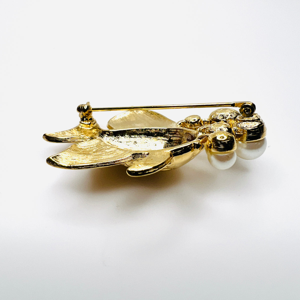 Side view of dimensional gold tone fish brooch with creamy faux pearls