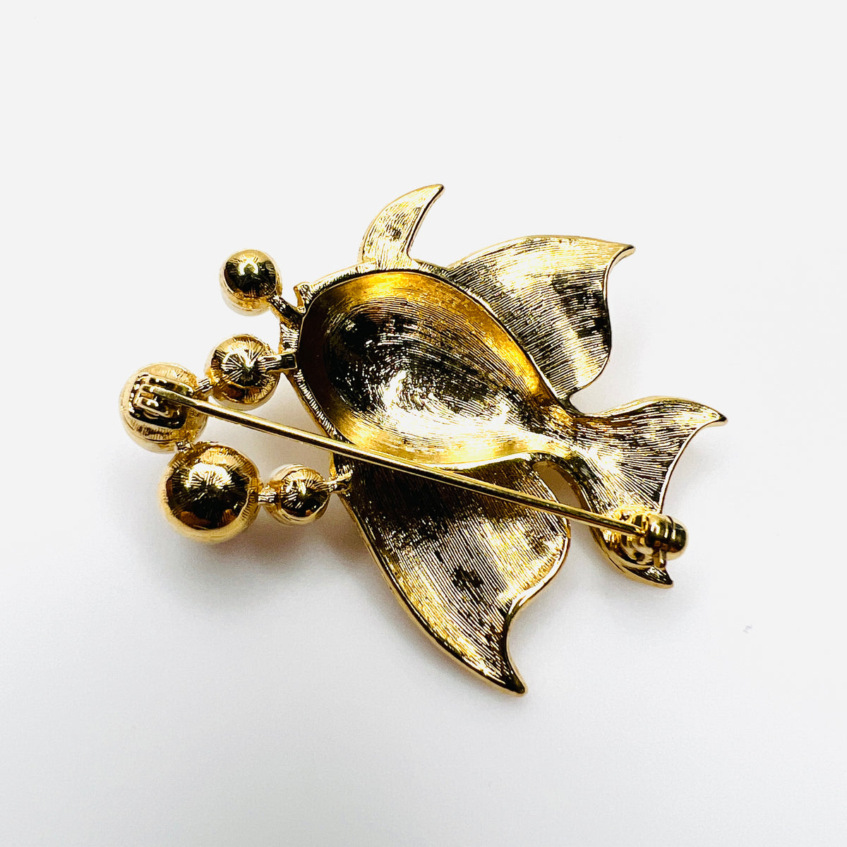 Reverse of vintage gold tone fish brooch showing pin back and textured fins