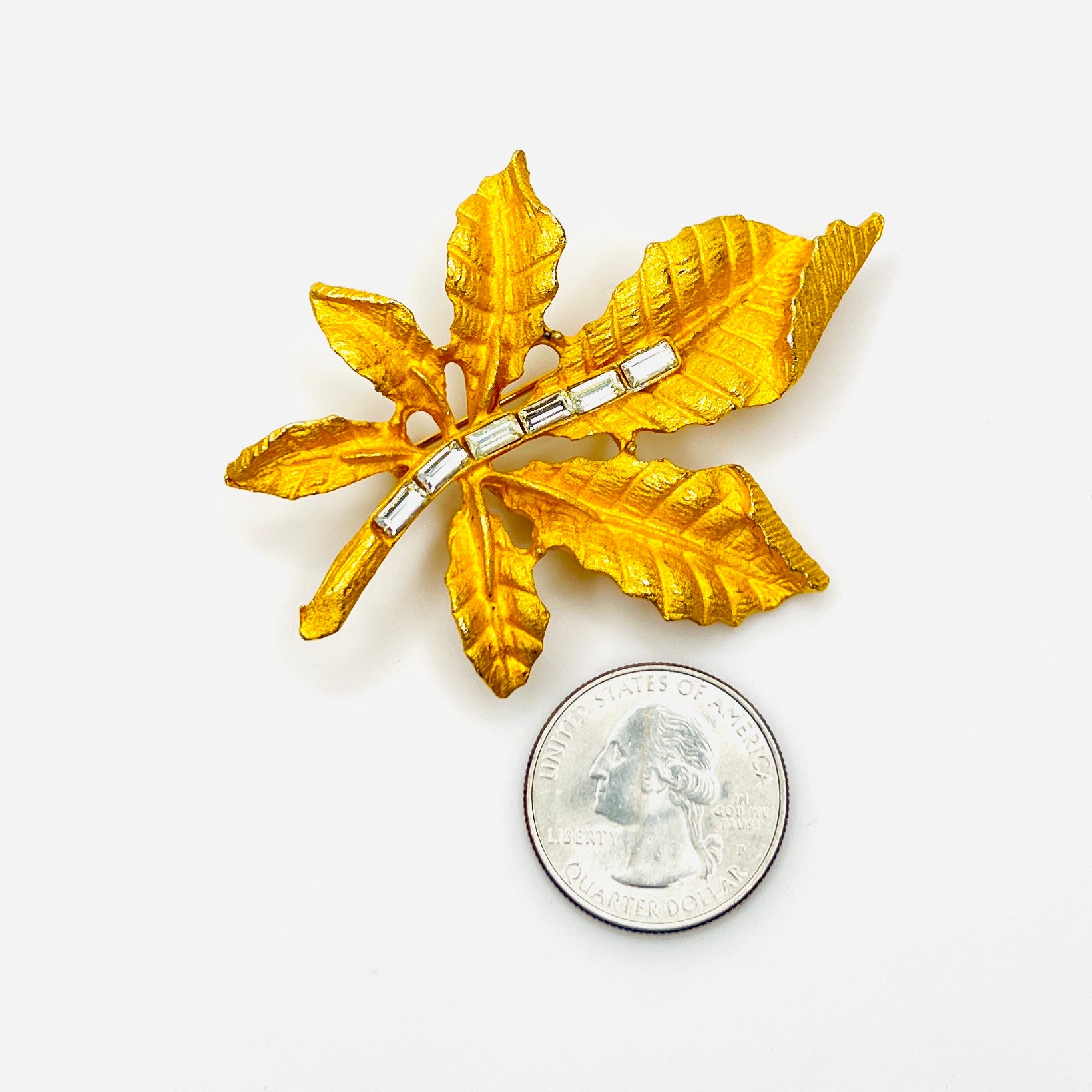 Gold tone botanical leaf brooch with rhinestones shown beside quarter for scale