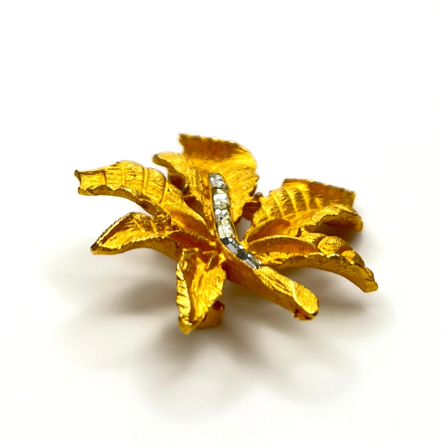Side profile of vintage textured gold tone leaf brooch with baguette rhinestones