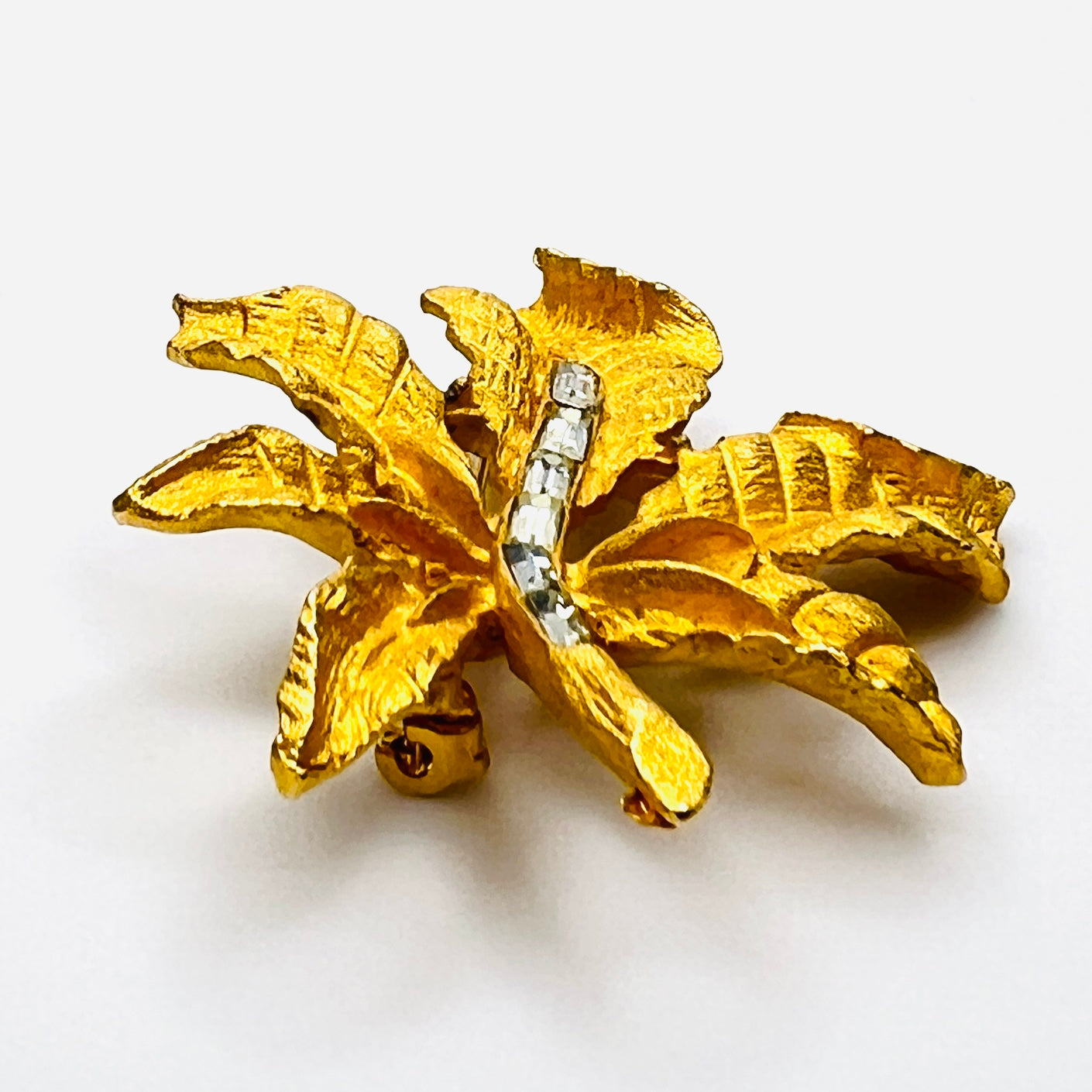Side profile of vintage textured gold tone leaf brooch with baguette rhinestones