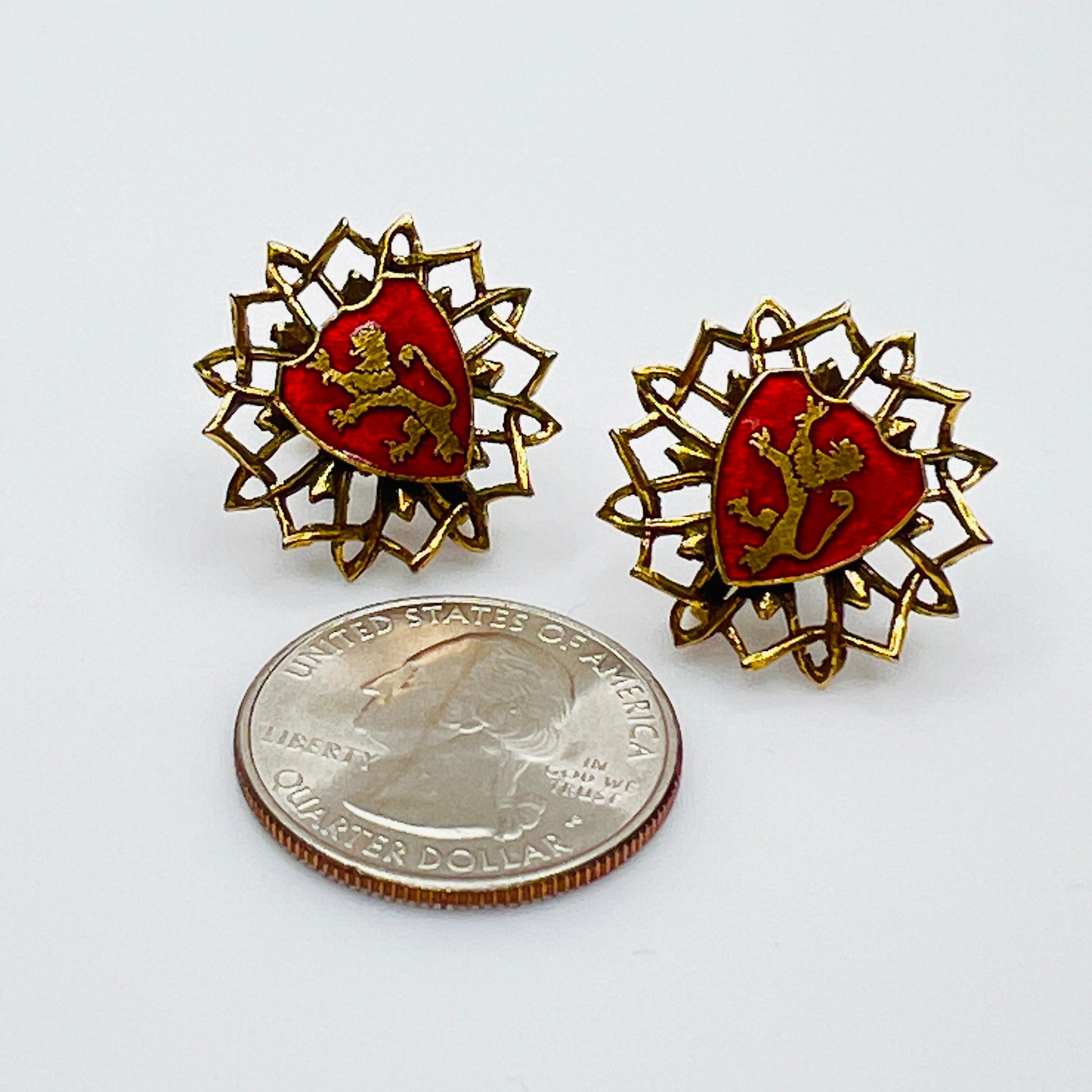 Red enamel coat of arms earrings beside quarter for scale