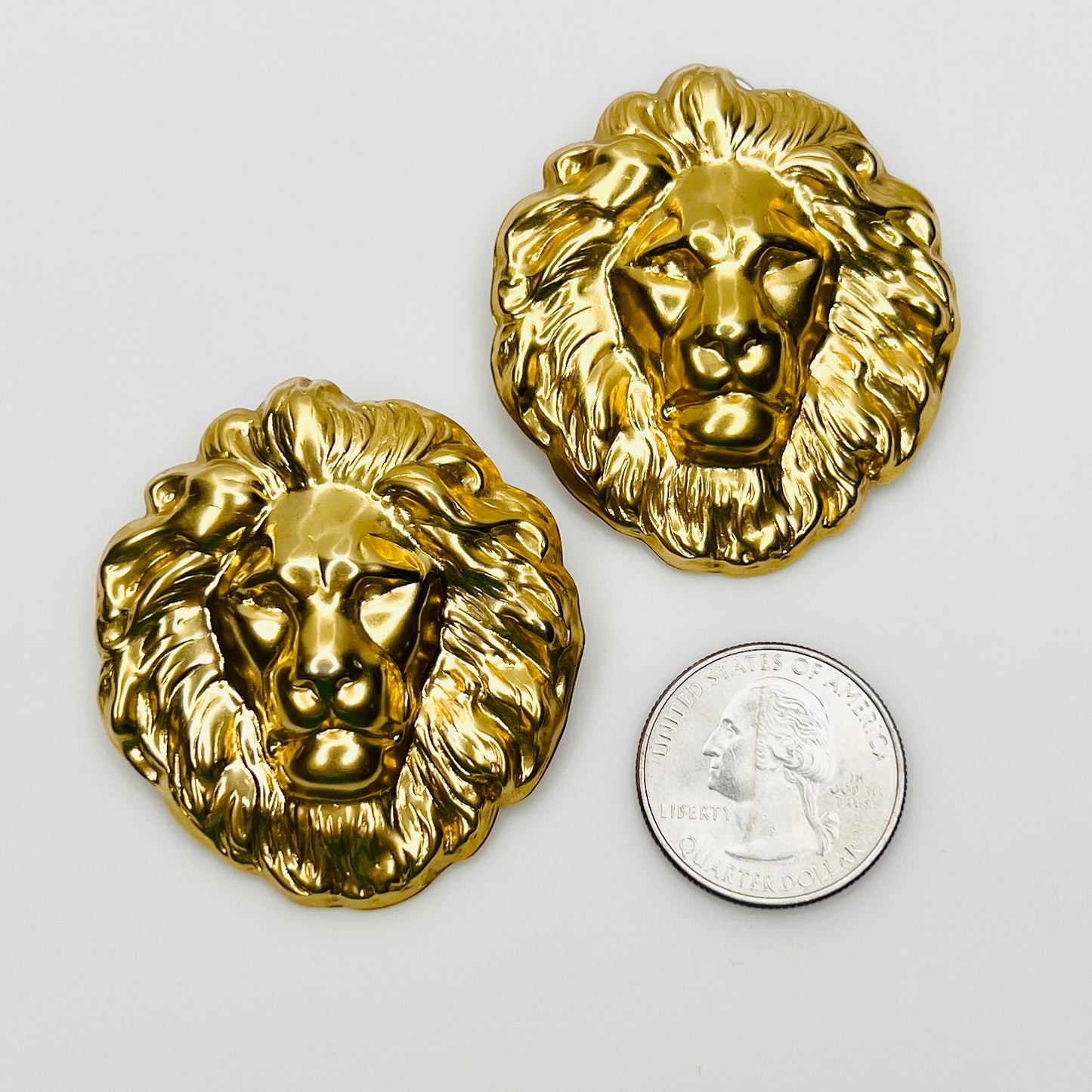 Gold tone lion head earrings beside quarter for scale