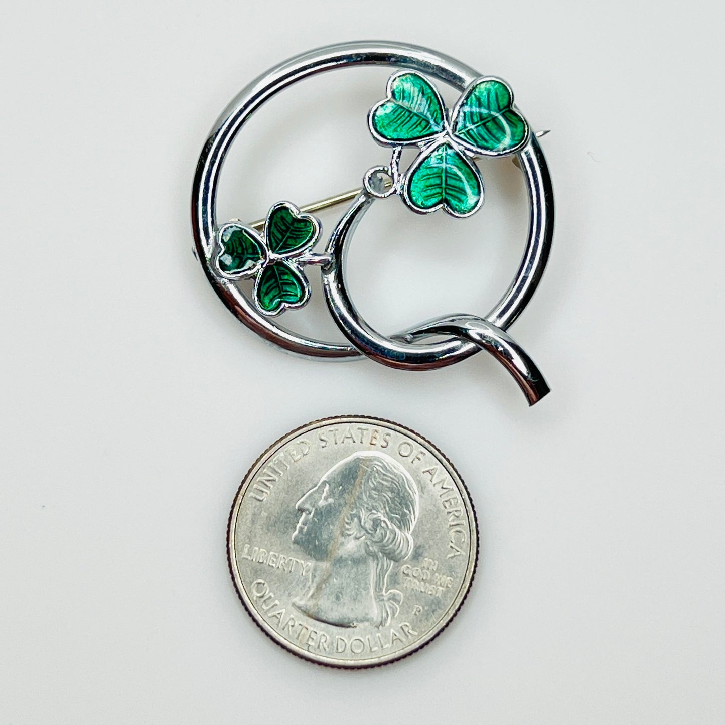 Signed Mizpah enamel shamrock brooch beside a U.S. quarter for size reference.