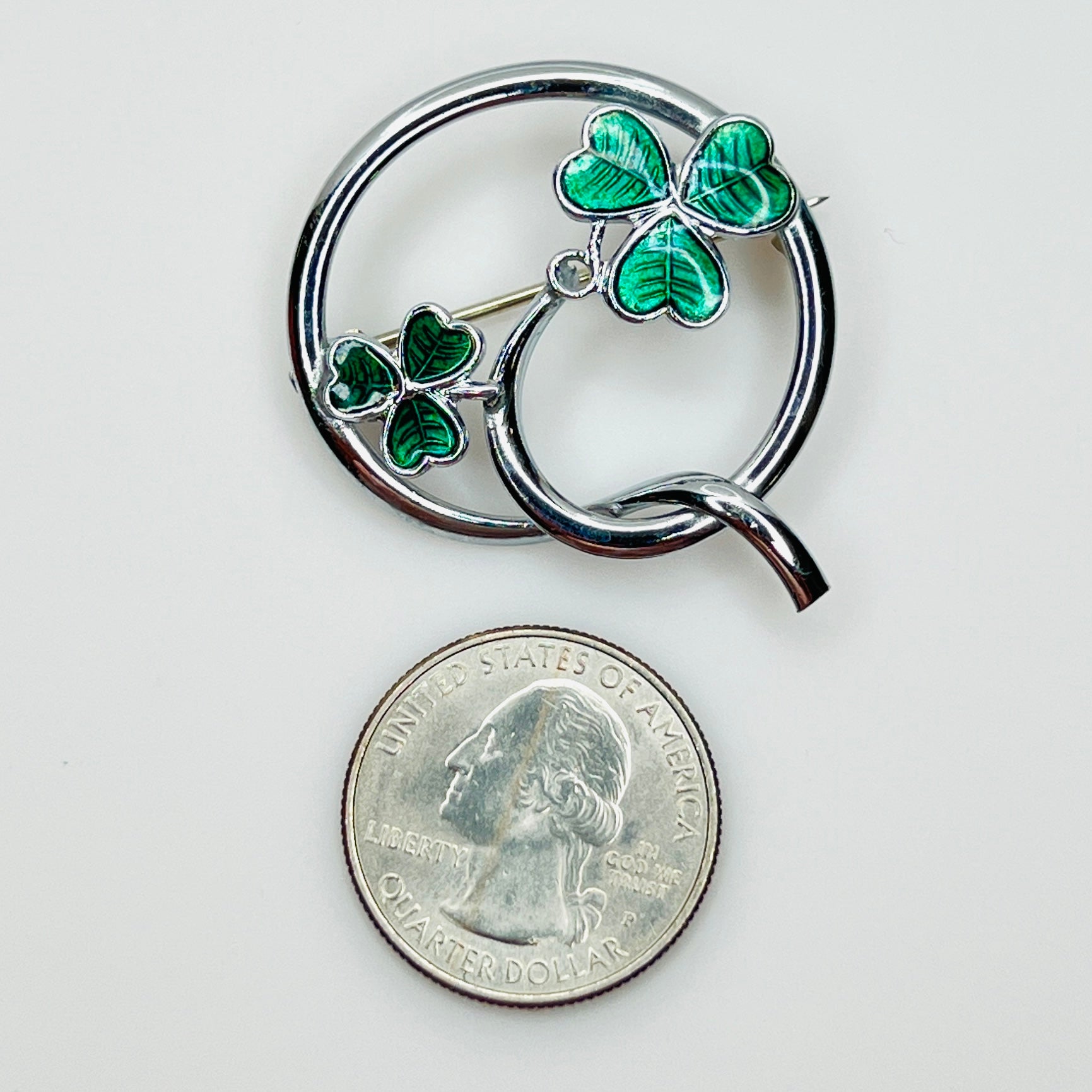 Signed Mizpah enamel shamrock brooch beside a U.S. quarter for size reference.