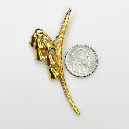 Signed Monet lily of the valley floral brooch beside quarter showing its elongated three-inch design