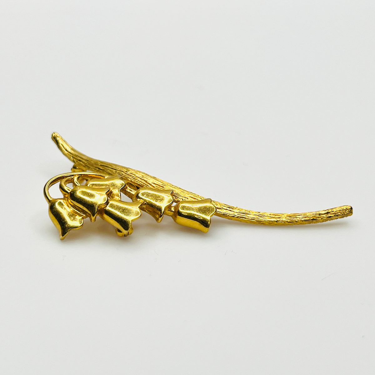 Side view of vintage gold-tone Monet flower brooch showing dimensional bell blossoms and textured stem