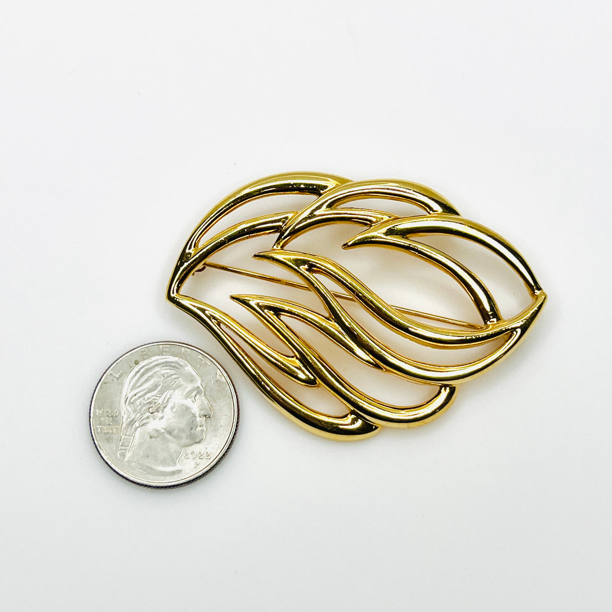 Signed Monet abstract gold-tone brooch beside quarter showing size and sculptural openwork design