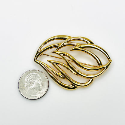 Signed Monet abstract gold-tone brooch beside quarter showing size and sculptural openwork design