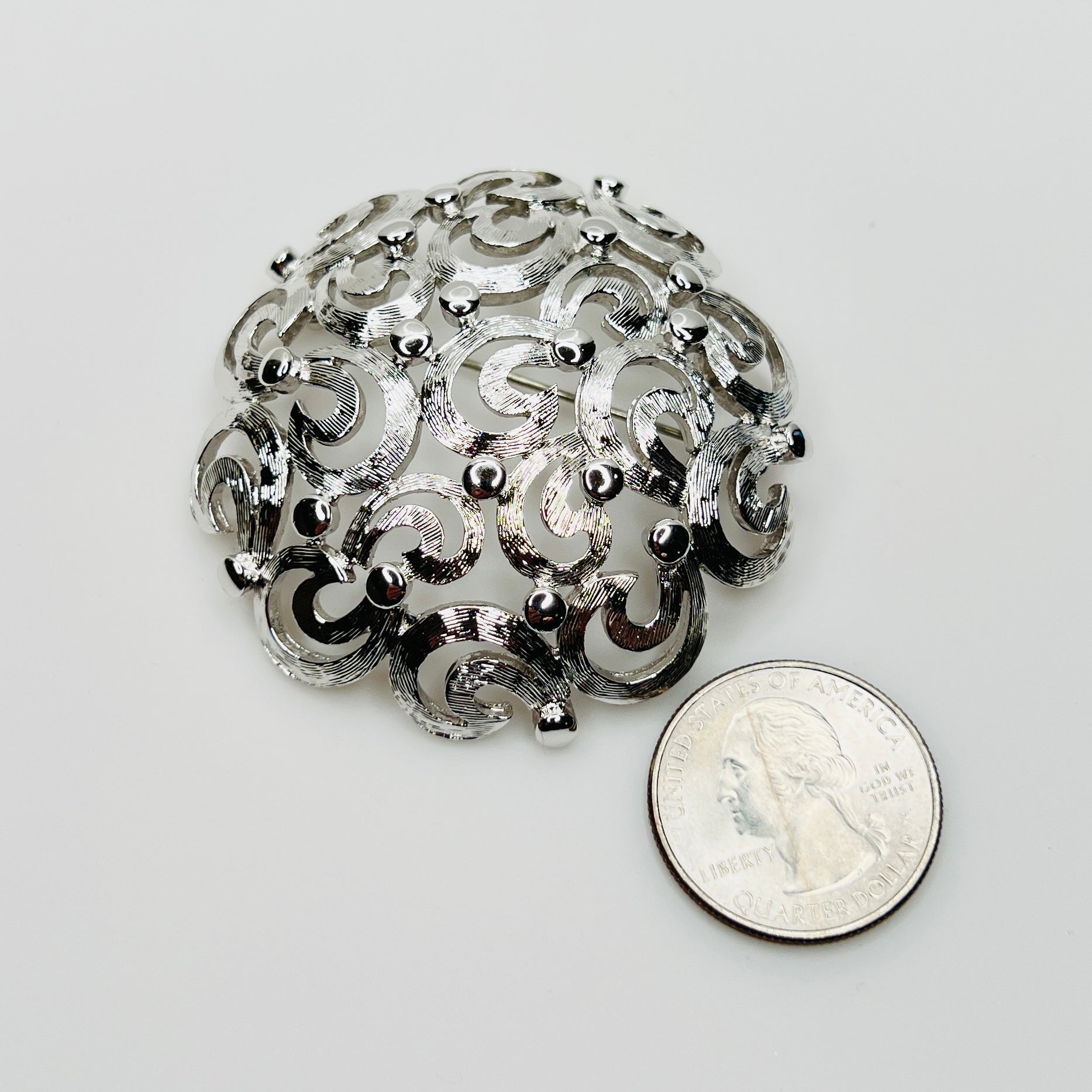 Silver tone Monet brooch next to coin for scale