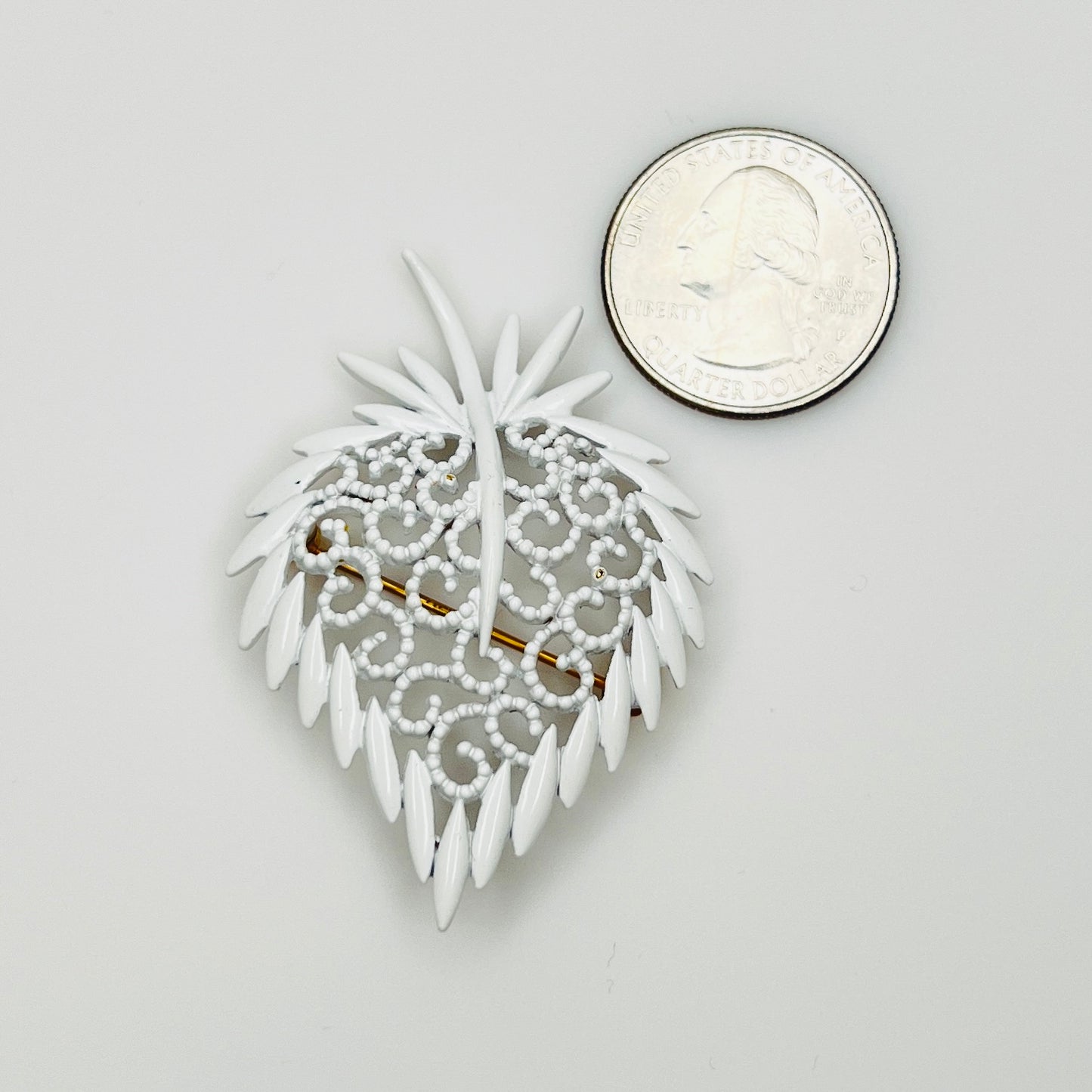 White enamel strawberry pin beside quarter for scale