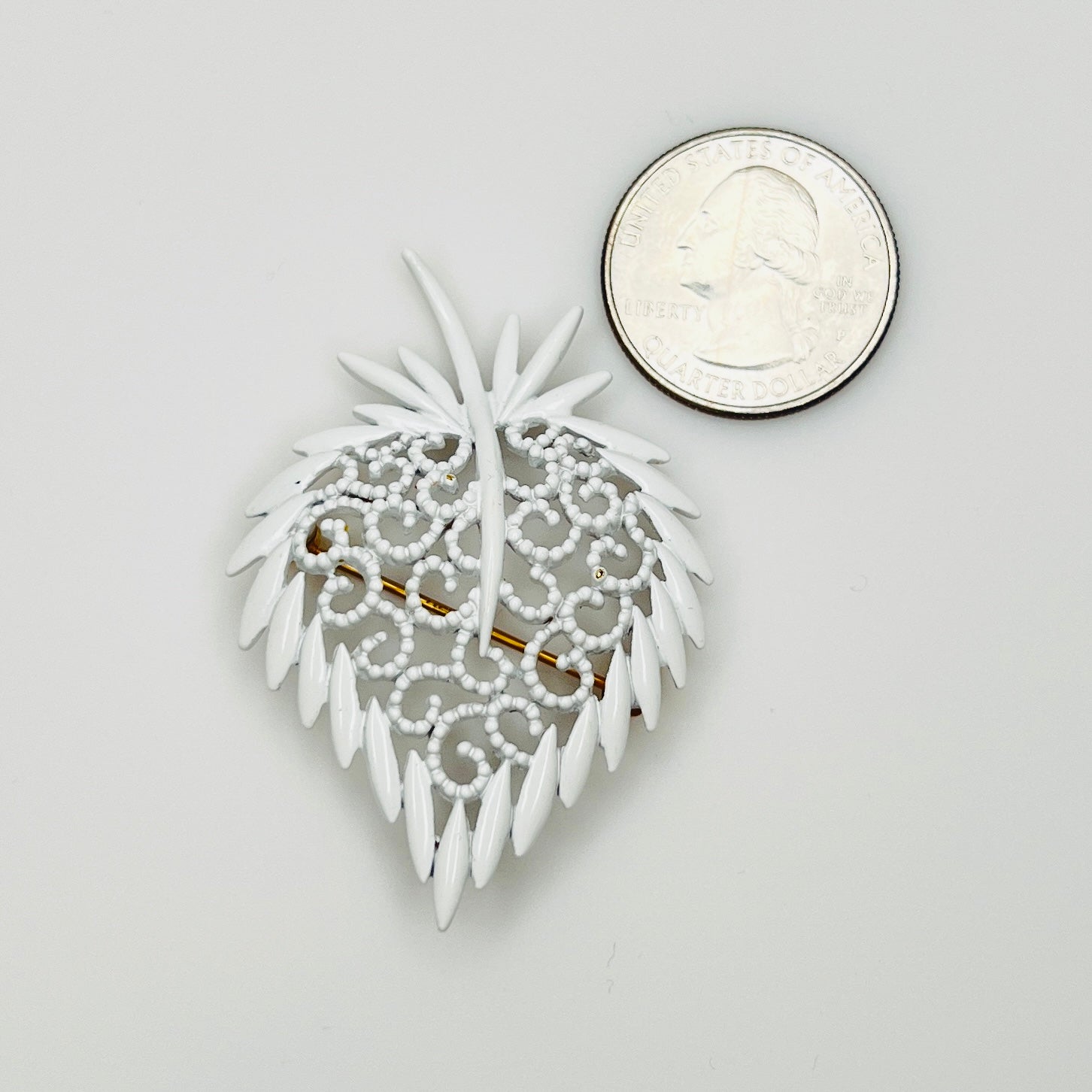 White enamel strawberry pin beside quarter for scale