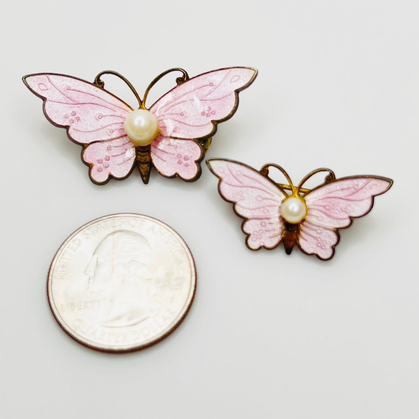 1950s pink butterfly brooch set with pearl accents shown beside quarter