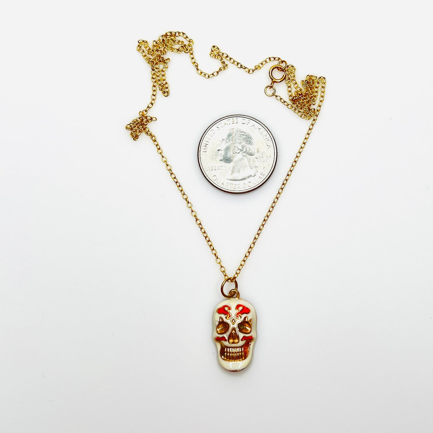 Enamel sugar skull pendant necklace beside quarter showing size and 20-inch chain.