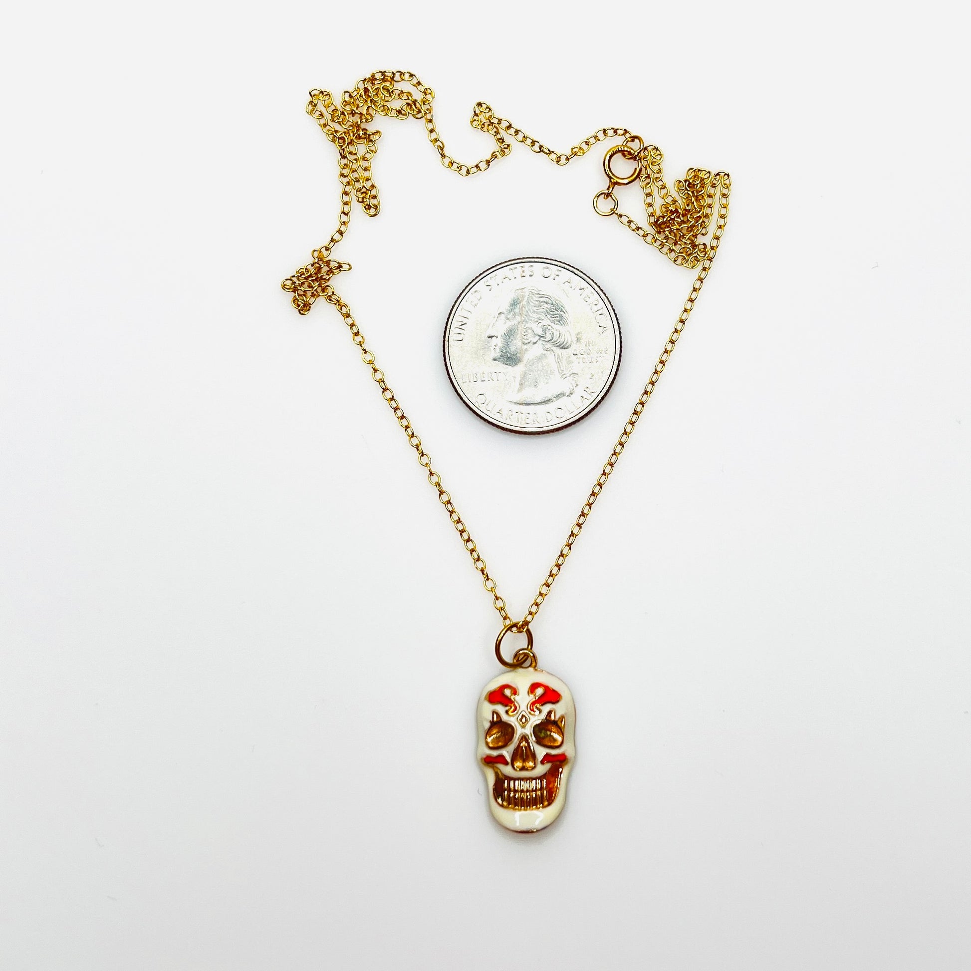 Enamel sugar skull pendant necklace beside quarter showing size and 20-inch chain.
