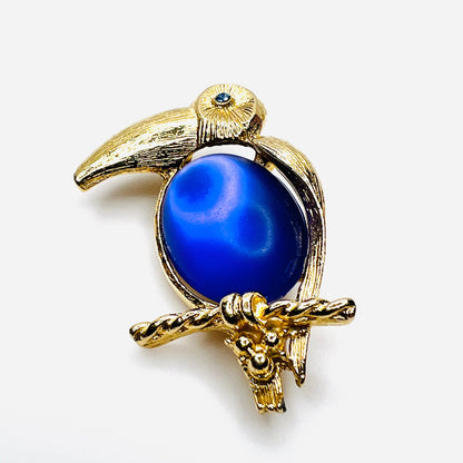 Close-up of gold-tone toucan brooch with luminous purple cabochon belly and rhinestone eye