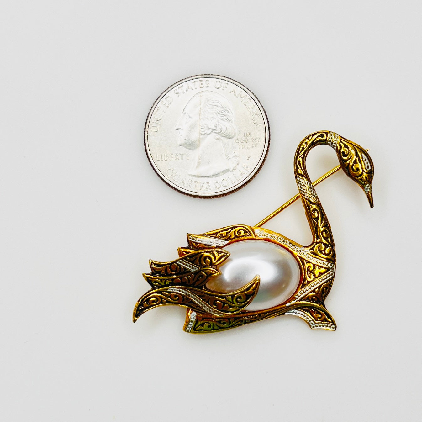 Spanish Damascene swan brooch beside quarter showing size reference