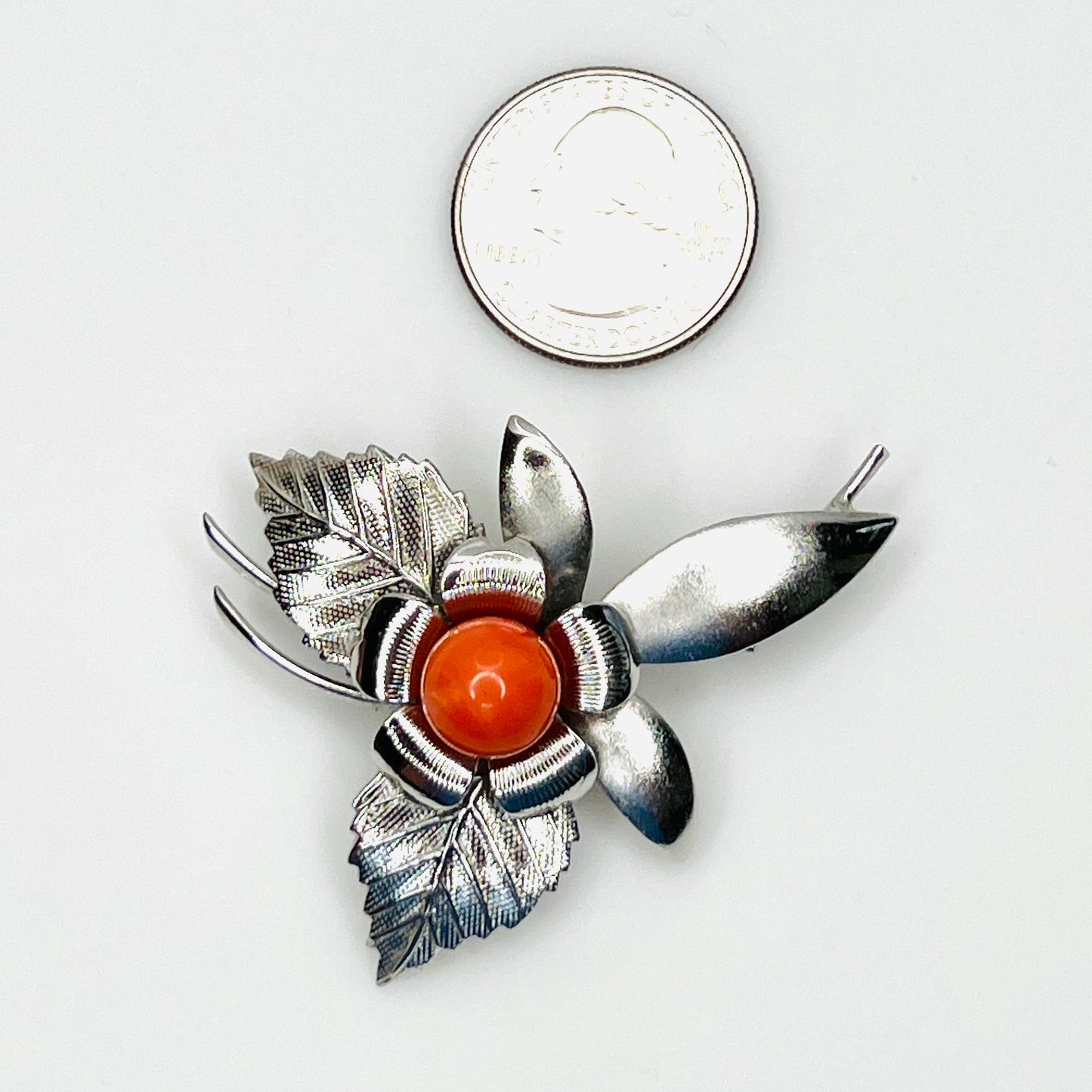 Modernist stainless steel floral brooch shown beside quarter for scale