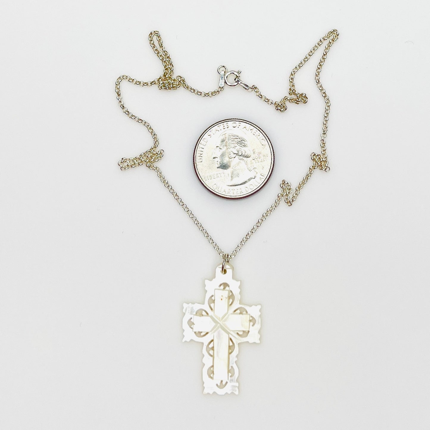 Hand-carved Mother of Pearl Bethlehem cross necklace with quarter for size comparison.