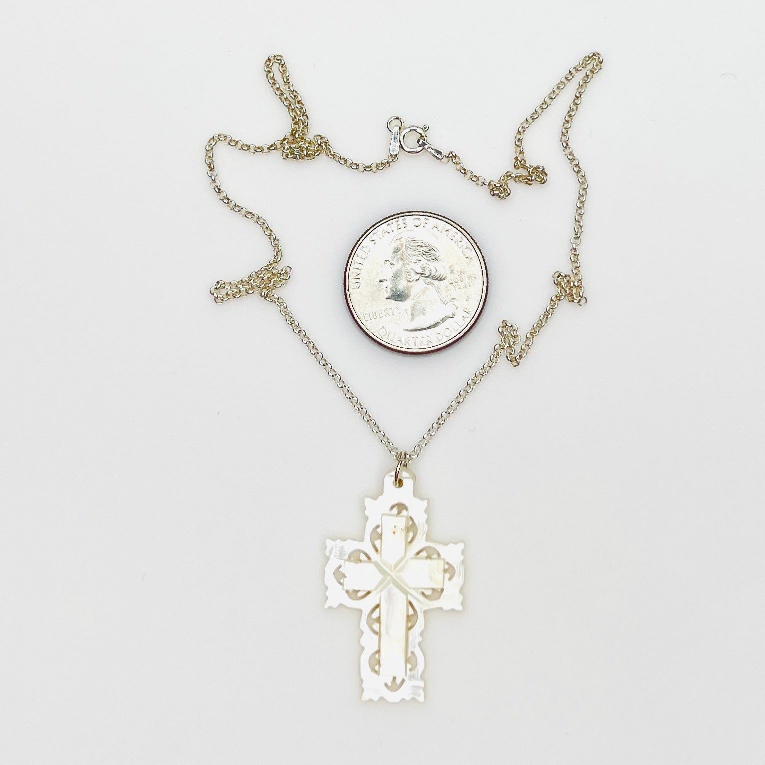 Hand-carved Mother of Pearl Bethlehem cross necklace with quarter for size comparison.