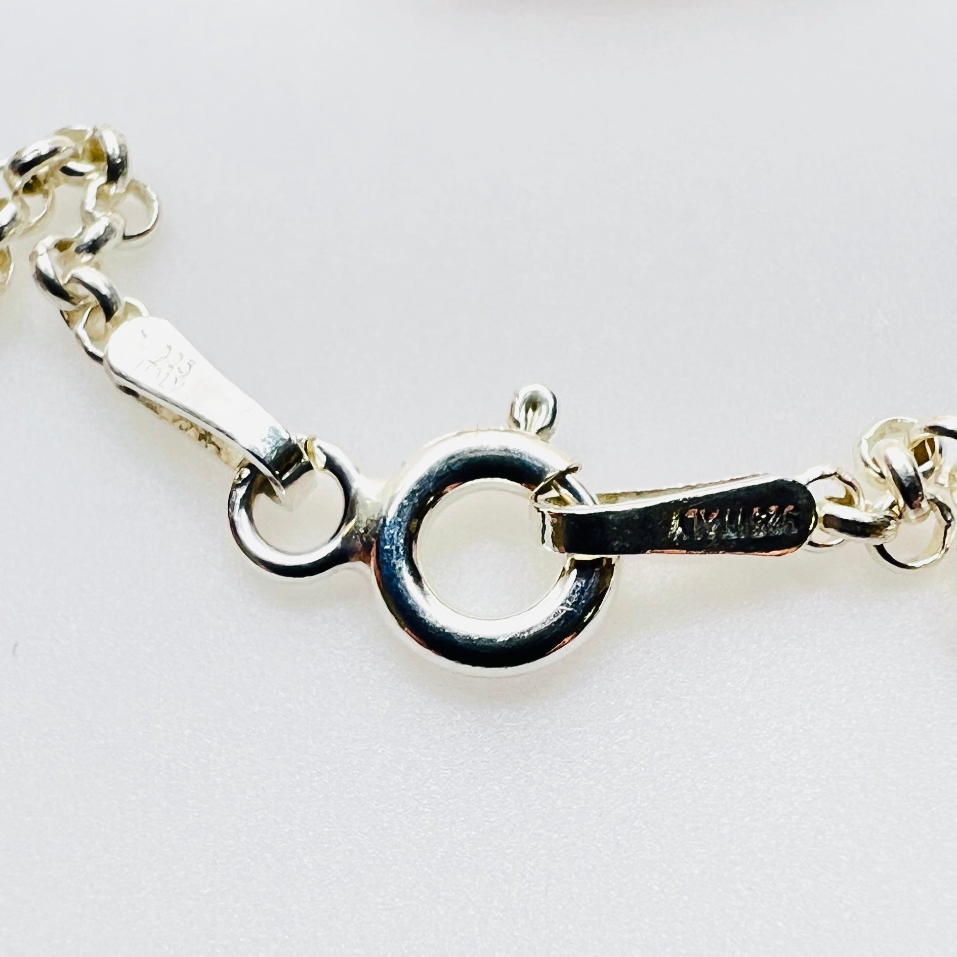 Close-up of a silver necklace chain clasp showing a lobster clasp with a circular ring and a tag engraved with Italy and 925.