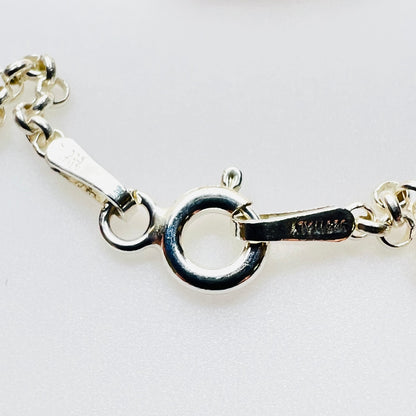 Close-up of a silver necklace chain clasp showing a lobster clasp with a circular ring and a tag engraved with Italy and 925.