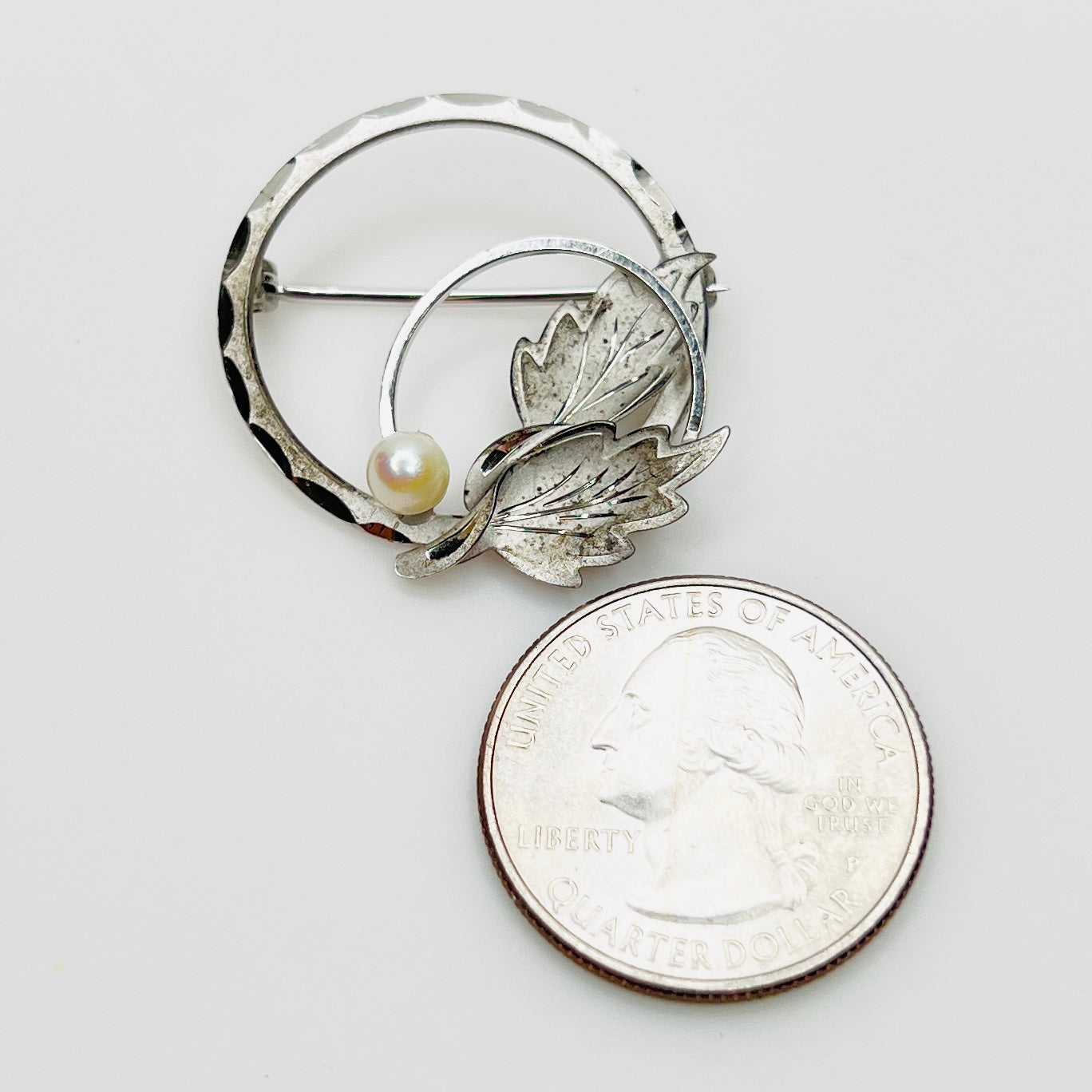DCE sterling silver pearl brooch shown beside quarter for scale