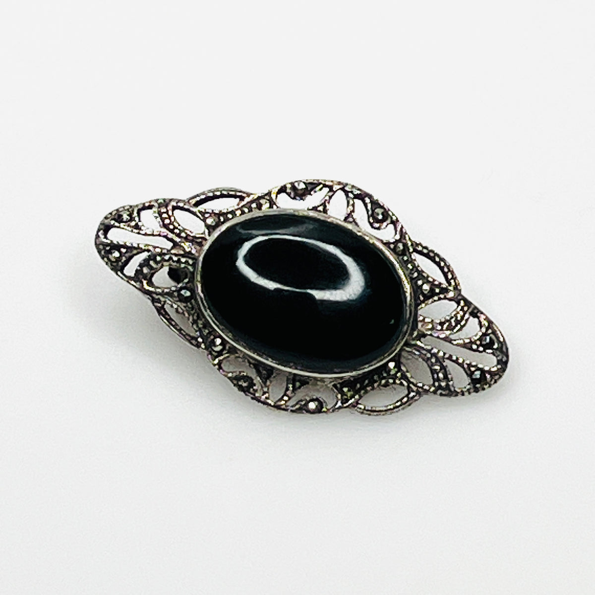 Vintage sterling silver brooch with oval black onyx cabochon, marcasite accents, and ornate filigree setting.