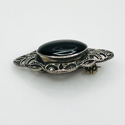 Angled view of vintage black onyx cabochon brooch showing raised bezel and intricate marcasite filigree.