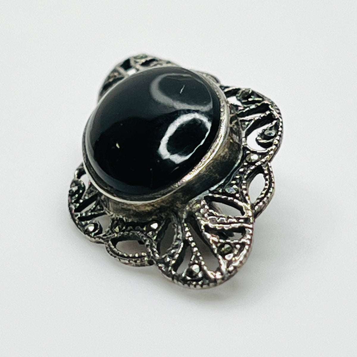 Angled view of vintage black onyx cabochon brooch showing raised bezel and intricate marcasite filigree.