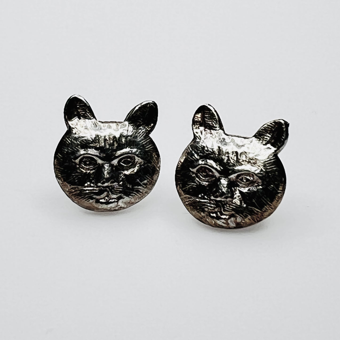 Close-up of silver cat earrings showing facial detail
