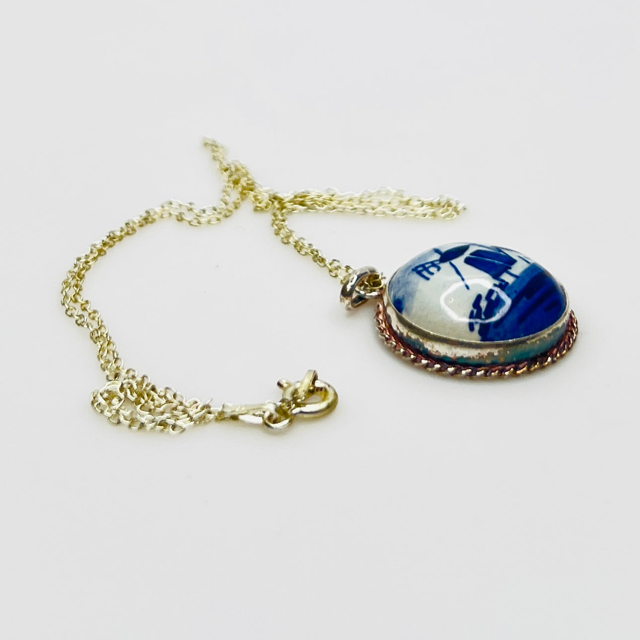 Side view of vintage Delft porcelain pendant in sterling silver setting on silver chain
