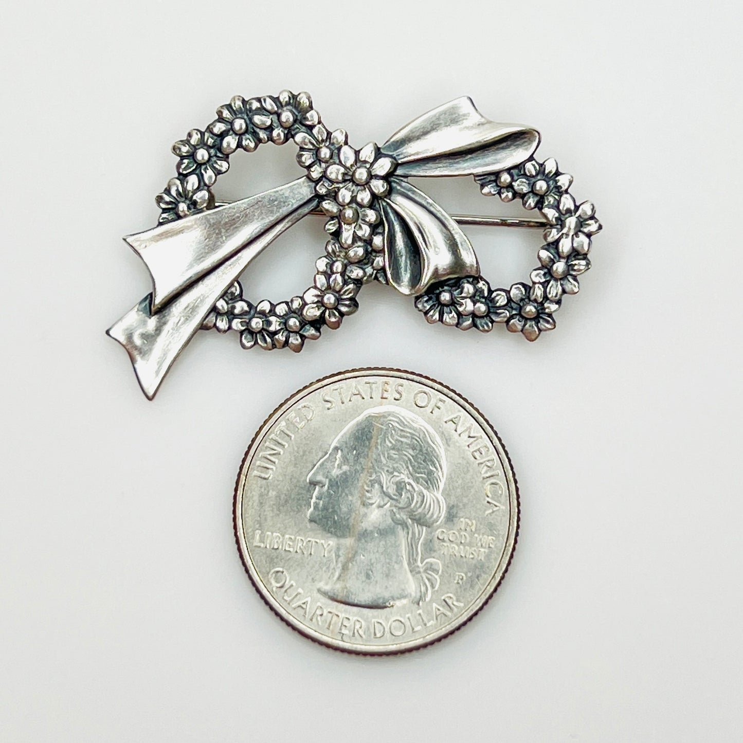 Sterling silver floral wreath bow brooch beside a U.S. quarter showing size.