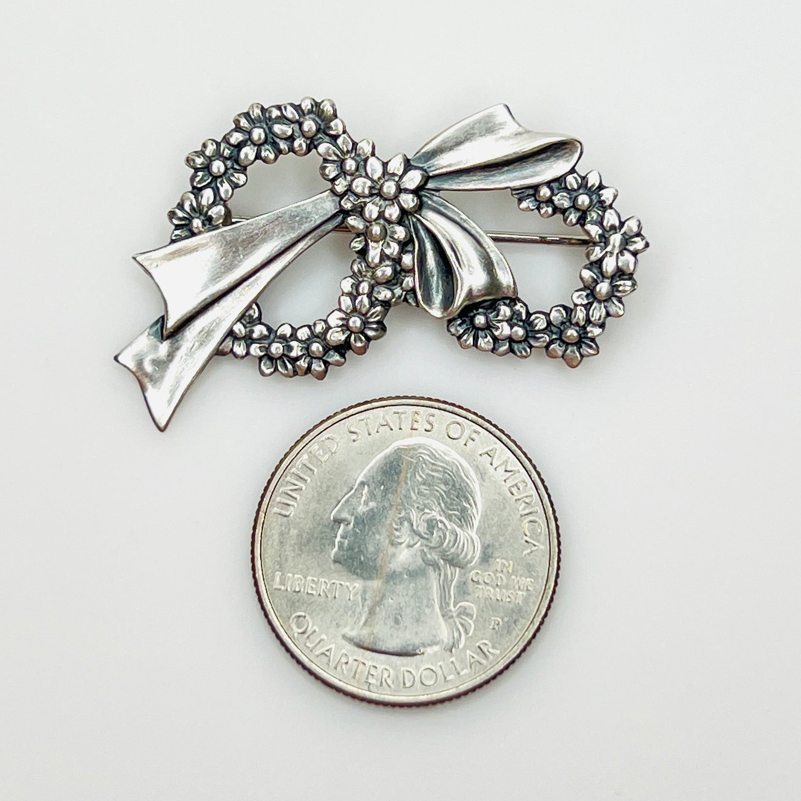 Sterling silver floral wreath bow brooch beside a U.S. quarter showing size.